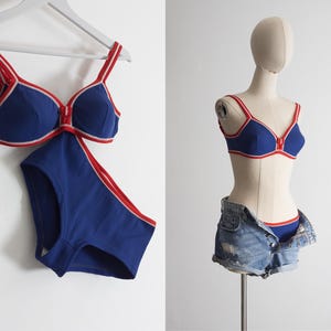 May include: A navy blue and red two-piece swimsuit. The bra and high-waisted bottoms have red trim. The swimsuit is displayed on a white hanger and on a mannequin wearing denim shorts.