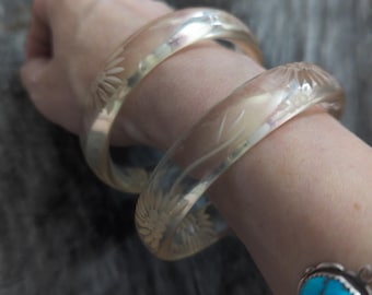 May include: Two clear plastic bangles with a floral design. The bangles are stacked on a person's wrist.