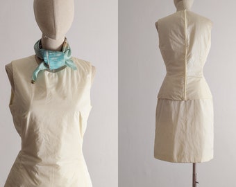 May include: A sleeveless, ivory dress with a fitted bodice and a full skirt. The dress has a cinched waist and a simple, elegant design.