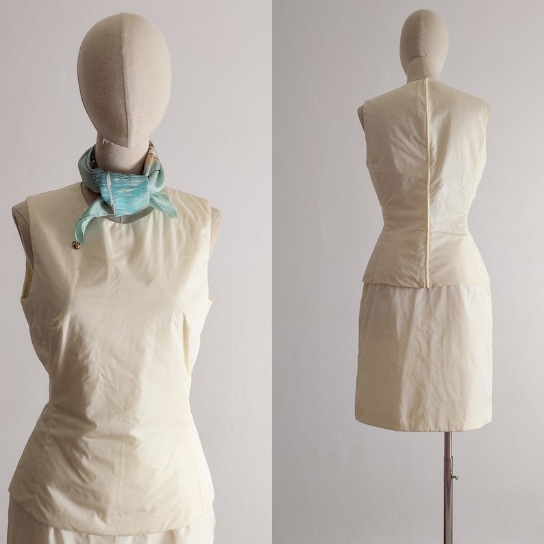 May include: A sleeveless, ivory dress with a fitted bodice and a full skirt. The dress has a cinched waist and a simple, elegant design.