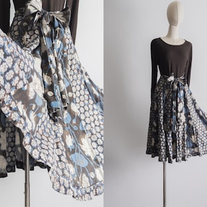 Puede incluir: Una falda de envoltura de estampado floral marrón y azul con una silueta larga y fluida. La falda tiene un dobladillo con volantes y un lazo en la cintura.