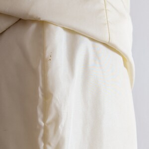 May include: Close-up of a white satin fabric with a slight crease. The fabric has a smooth, silky texture.