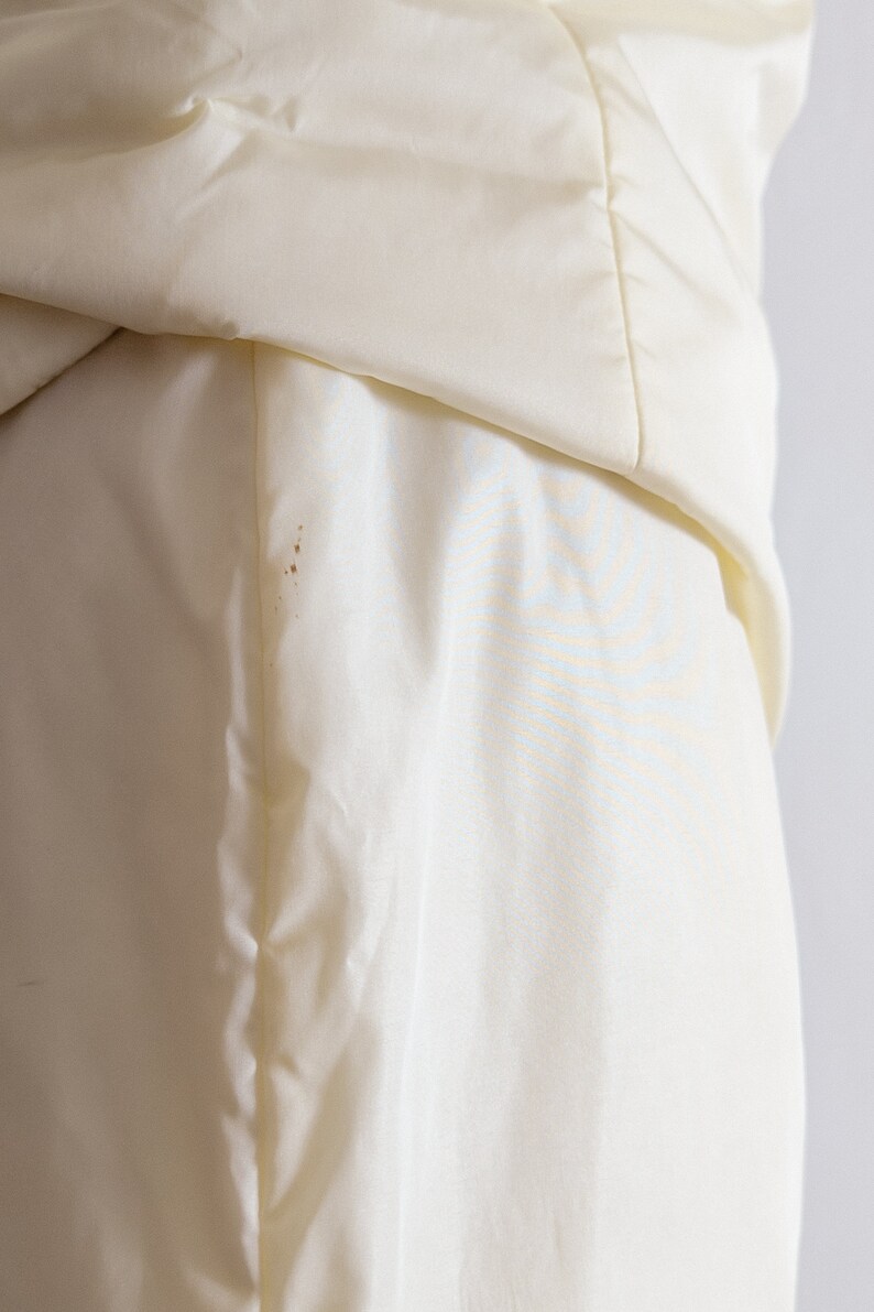 May include: Close-up of a white satin fabric with a slight crease. The fabric has a smooth, silky texture.