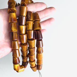 以下が含まれることがあります： 緑色の紐に、茶色と黄色の円錐形のビーズが通されたネックレス。ビーズは木や骨などの天然素材で作られている可能性があります。