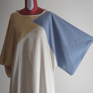 Op de afbeelding: Een loszittende, lange tuniekjurk met een geometrisch patroon in beige, wit en blauw. De jurk heeft een wijde, vloeiende silhouet en een ronde hals.