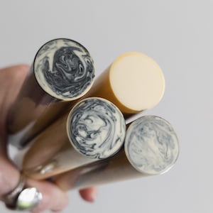 Puede incluir: Cuatro varillas cilíndricas sostenidas juntas, que incluyen dos varillas de color crema sólido y dos varillas con un patrón de remolinos de mármol blanco y negro en sus extremos circulares. Las varillas tienen superficies lisas y pulidas.