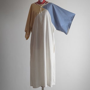 Op de afbeelding: Een losse jurk met korte mouwen in de kleuren wit, geel en blauw. De jurk heeft een strik aan de halslijn.