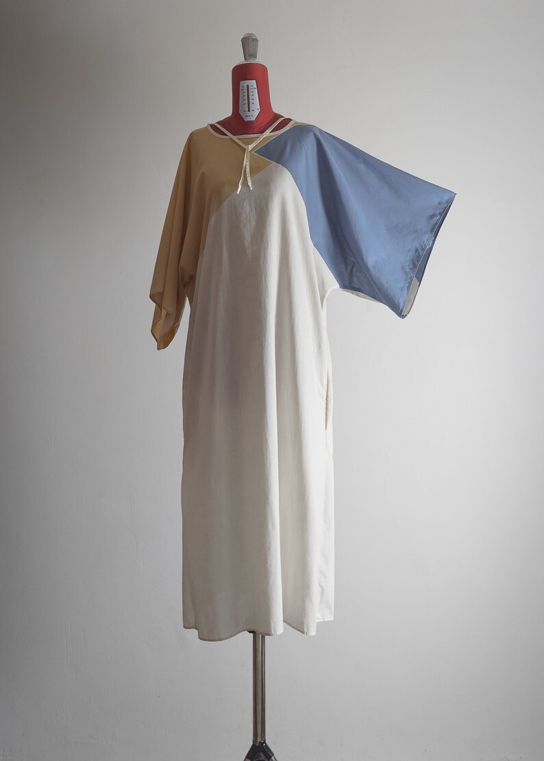 Op de afbeelding: Een losse jurk met korte mouwen in de kleuren wit, geel en blauw. De jurk heeft een strik aan de halslijn.
