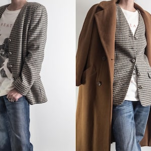 May include: A houndstooth blazer and vest paired with a white graphic tee and blue jeans. A long brown coat is draped over the outfit. The tee features a black and white graphic with the text "BEAT" and "ROAD".