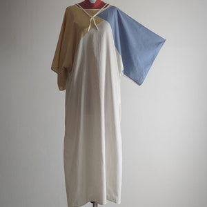 Op de afbeelding: Een witte, gele en blauwe kleurblokjurk met een strik aan de hals. De jurk heeft een losse pasvorm en is gemaakt van een lichtgewicht stof.