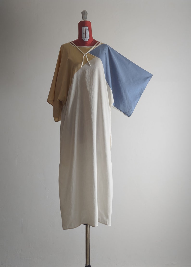 Op de afbeelding: Een witte, gele en blauwe kleurblokjurk met een strik aan de hals. De jurk heeft een losse pasvorm en is gemaakt van een lichtgewicht stof.