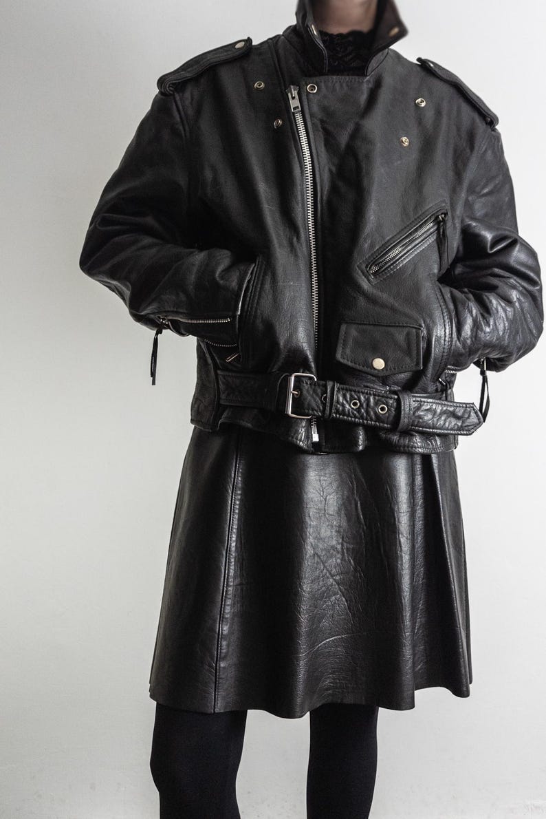 May include: Black leather jacket with a belted waist and a matching black leather skirt. The jacket features a zipper closure, multiple pockets, and shoulder epaulets. The skirt is a flared style.