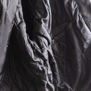 May include: Close-up of a black leather jacket interior. The quilted lining is visible, along with the smooth, shiny fabric of the jacket's interior. The jacket appears to be well-worn.