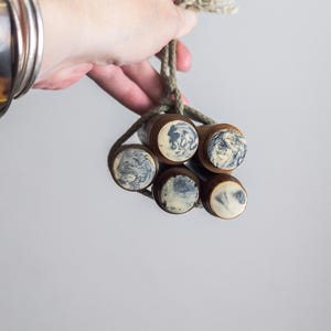 May include: Six wooden bottle stoppers with marbled white and blue tops, joined by a rope. The stoppers have a dark brown finish. The image is set against a plain white background.