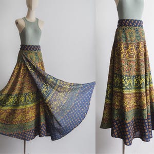 May include: A long, flowing skirt with a vibrant, patterned design. The skirt features a mix of yellow, green, and blue hues with intricate motifs. The waistband is a dark blue with a repeating pattern. The skirt is displayed on a mannequin.