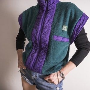 May include: A teal and purple quilted vest with a zipper closure and a small logo patch. The vest has a high collar and a sleeveless design.