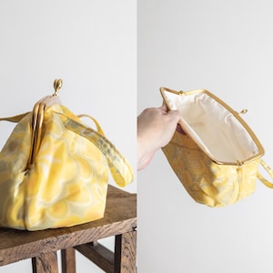 Può includere: Borsa a mano gialla vintage con chiusura e manici dorati. La borsa presenta un motivo floreale nei toni del giallo e del verde. L'interno è foderato in tessuto color crema. La borsa è su uno sgabello di legno. Circa 25 cm.