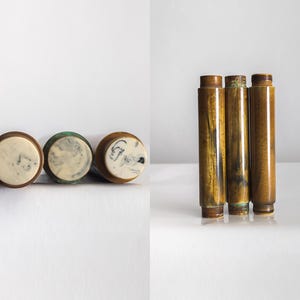 Puede incluir: Tres tapones de botella con la parte superior de color crema y base de madera marrón. Las tapas tienen un diseño veteado. También se muestran tres objetos cilíndricos marrones con un acabado brillante, posiblemente elementos decorativos o partes de un conjunto.