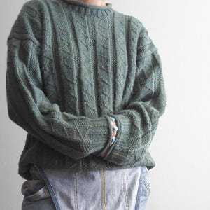 May include: A green knitted sweater with a diamond pattern. The sweater has long sleeves and a crew neck.