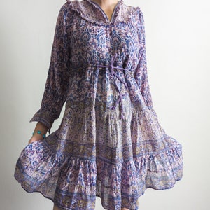 Puede incluir: Un vestido de manga larga con cuello de volantes y falda de capas, estampado con flores moradas y azules.
