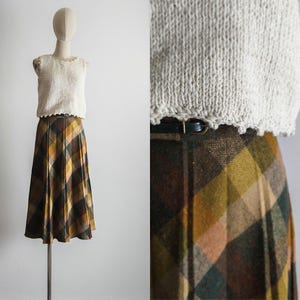 May include: A brown, green, and yellow plaid skirt with a black belt. The skirt is pleated and has a mid-length hemline.