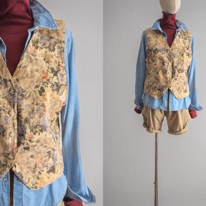Könnte beinhalten: Eine beige Weste mit floralem Muster über einem blauen Jeanshemd. Die Weste hat einen Knopfverschluss und einen spitzen Kragen.