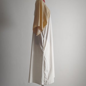 Op de afbeelding: Een witte en beige jurk met een korte mouw op een mannequin. De jurk heeft een losse pasvorm en een eenvoudig ontwerp.