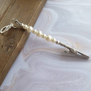 May include: A white pearl and silver clip-on charm with a silver clasp. The charm is made of faux pearls and a silver metal clip.