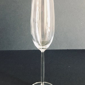 May include: A clear glass champagne flute with a long stem and a wide base.