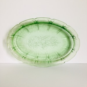 May include: A vintage green glass oval serving platter with a raised floral design. The platter has a scalloped edge and is perfect for serving snacks or appetizers.