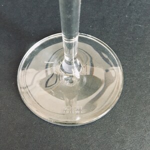 May include: Close-up of the base of a clear glass wine glass with the text "SCHOTT ZWIESEL" printed on the bottom.