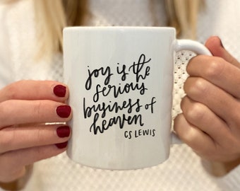 May include: White ceramic mug with black handwritten text that reads "joy is the serious business of heaven" and "C.S. Lewis" in smaller font.