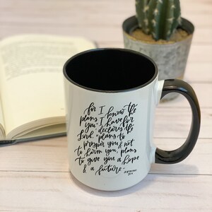 May include: White ceramic mug with a black handle and black interior. The mug has a black handwritten quote on it that reads "for I know the plans I have for you, declares the Lord, 'plans to prosper you & not to harm you, plans to give you a hope & a future.'"  Jeremiah 29:11