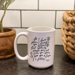 May include: White ceramic mug with a black inspirational quote from Jeremiah 29:11. The quote reads "for I know the plans I have for you, declares the Lord. "plans to prosper you & not to harm you, plans to give you a hope & a future."