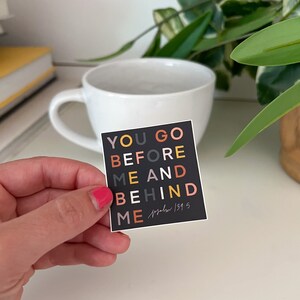May include: A black square sticker with the text "YOU GO BEFORE ME AND BEHIND ME" in colourful letters. The text "Psalm 139:5" is written in a smaller font below the main text.
