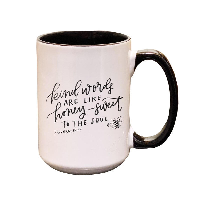 May include: White ceramic mug with a black handle and black interior. The mug features a black and white illustration of a bee and the text "kind words are like honey-sweet to the soul Proverbs 16:24".