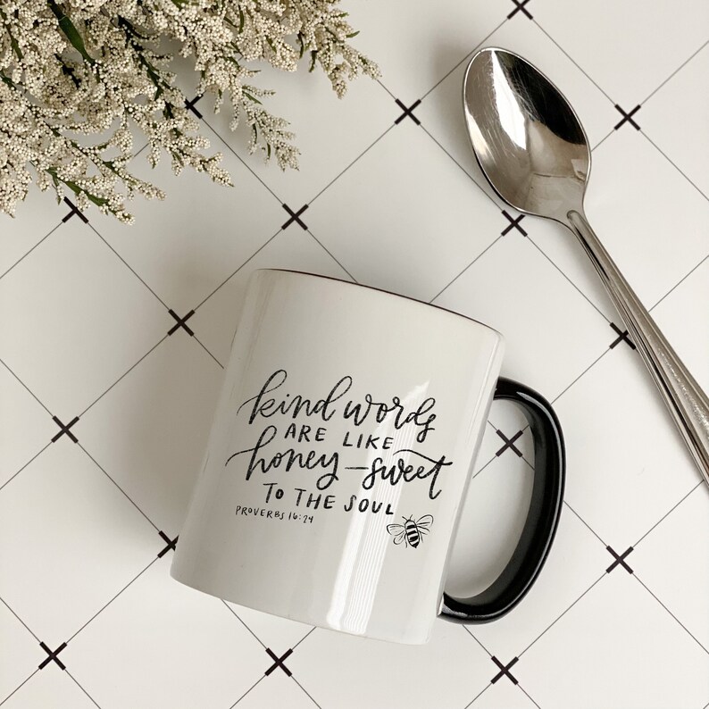 May include: White ceramic mug with a black handle. The mug has a black design that says "Kind words are like honey-sweet to the soul" with a bee graphic and the text "Proverbs 16:24".