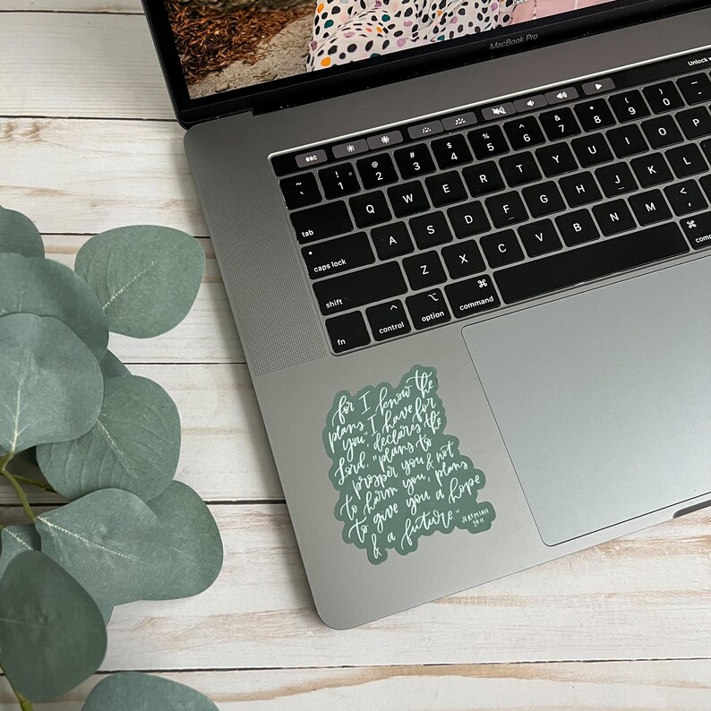 May include: A green sticker with white lettering on a silver laptop. The sticker features a quote from the Bible: "For I know the plans I have for you," declares the Lord, "plans to prosper you and not to harm you, plans to give you hope and a future."