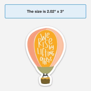 May include: A sticker of a hot air balloon with the text "We Rise by Lifting Others". The balloon is pink and yellow with a green basket. The sticker is 5.1 cm by 7.6 cm.