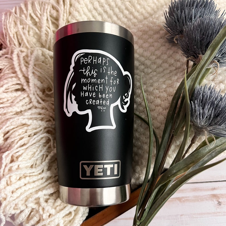 May include: Black Yeti tumbler with a white vinyl sticker that says "Perhaps this is the moment for which you have been created." The sticker features a silhouette of a woman's head.