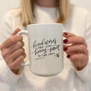 May include: White ceramic mug with a black handwritten quote that reads "Kind words are like honey-sweet to the soul" with a bee illustration and the scripture reference "Proverbs 16:24".