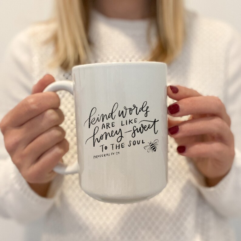 May include: White ceramic mug with a black handwritten quote that reads "Kind words are like honey-sweet to the soul" with a bee illustration and the scripture reference "Proverbs 16:24".
