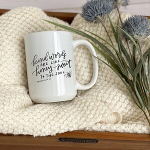 May include: White ceramic mug with a black handwritten quote that reads "Kind words are like honey-sweet to the soul" with a small bee illustration and the scripture reference "Proverbs 16:24".