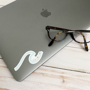 May include: A silver laptop with a sticker that says "Live Aloha" in rainbow colors on a wave design. A pair of tortoiseshell glasses are on top of the laptop.