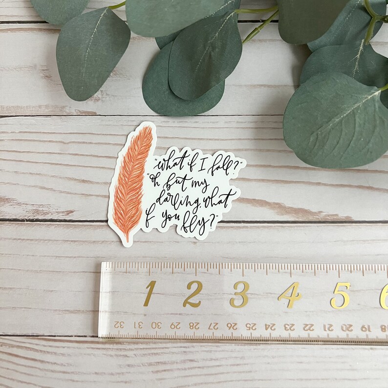 Op de afbeelding: Een sticker met een oranje veer en de tekst "what if I fall? oh but my darling, what if you fly?"
