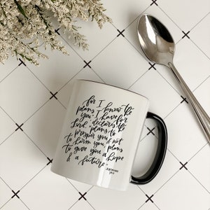 May include: White ceramic mug with a black handle. The mug features a black handwritten quote: "For I know the plans I have for you," declares the Lord, "plans to prosper you and not to harm you, plans to give you hope and a future." The quote is attributed to Jeremiah 29:11.
