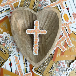 May include: A wooden heart-shaped dish with a floral cross sticker on it. The dish is surrounded by various stickers with floral designs and text, including "You are", "Hard Times", and "Prayer".