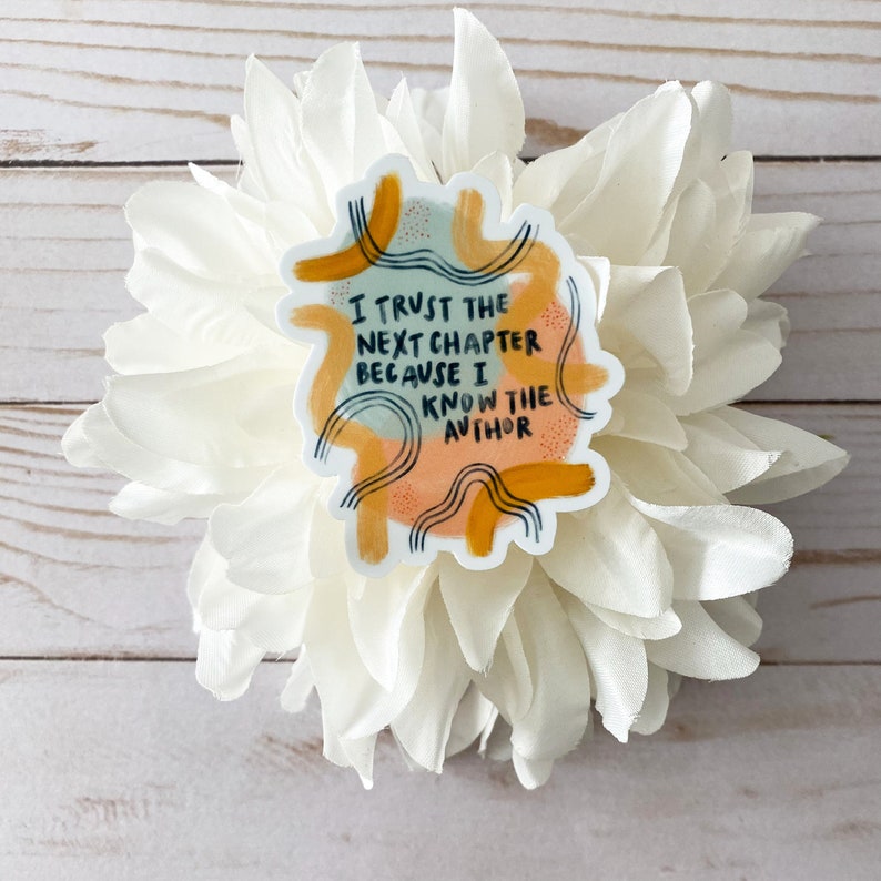 May include: A sticker with an abstract design in shades of yellow, orange, and blue. The sticker features the text "I trust the next chapter because I know the author."