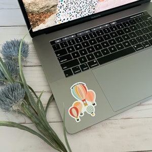 May include: A laptop computer with a sticker on the bottom right corner. The sticker features a hot air balloon with the text "#prettyvibesalways".
