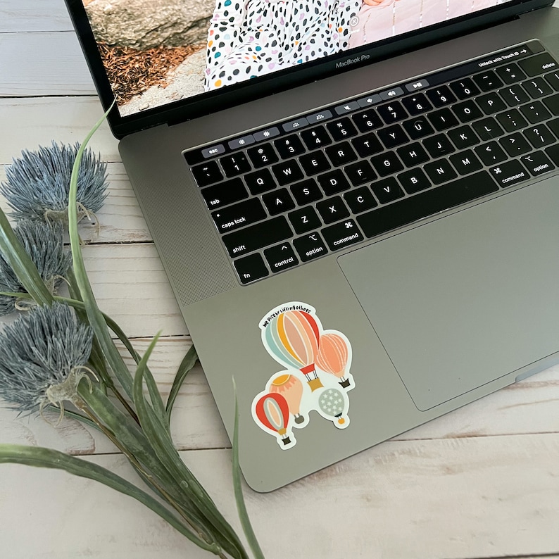 May include: A laptop computer with a sticker on the bottom right corner. The sticker features a hot air balloon with the text "#prettyvibesalways".
